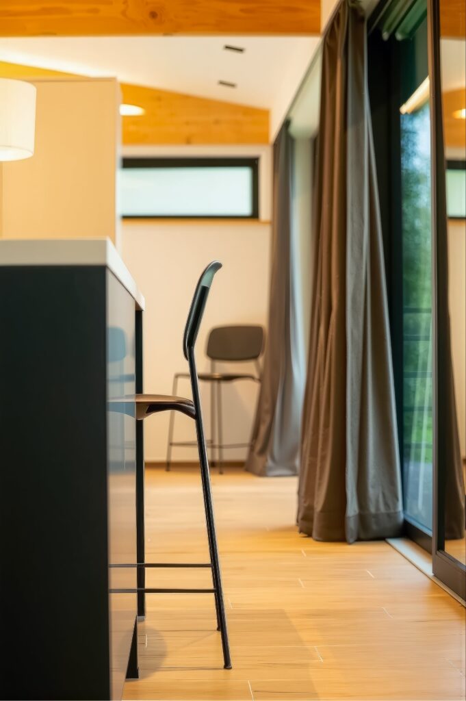 Détail d'ambiance : tabouret de bar design noir le long du comptoir de cuisine, mettant en valeur le contraste avec le sol en bois clair.