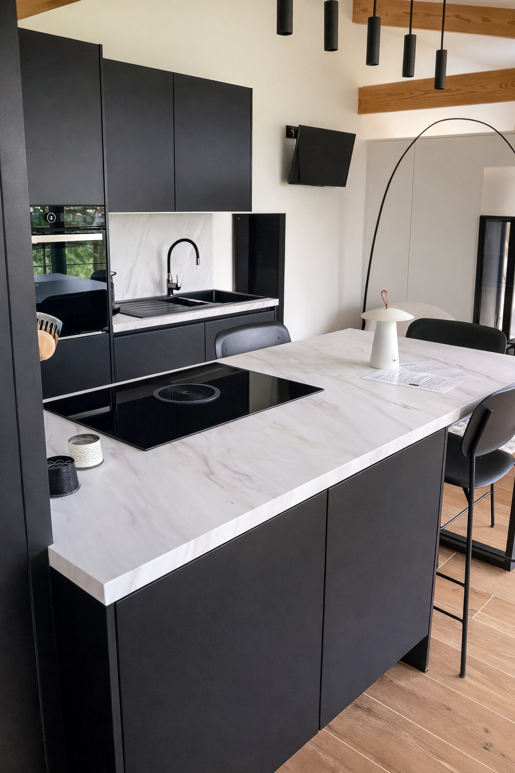 Plan de travail effet marbre blanc contrastant avec un évier noir mat et une taque de cuisson à hotte intégrée. Finitions haut de gamme K-Lita.